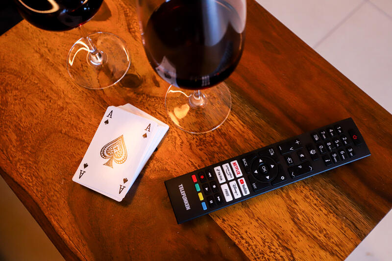 Smart-TV-Fernbedienung, Spielkarten und Weingläser auf Holztisch